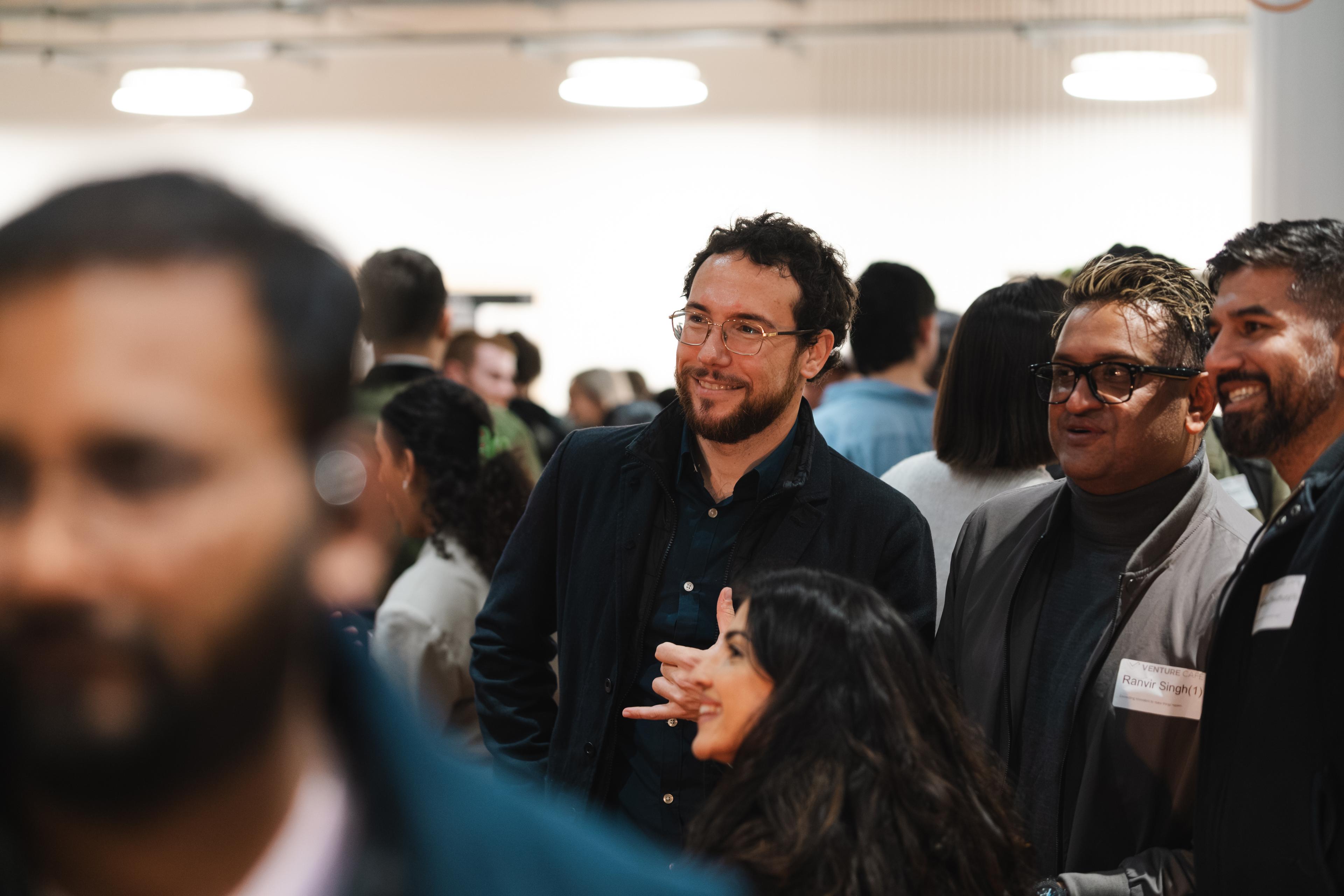 A crowd of smartly dressed people, people wearing name badges and looking in the same direction smiling.