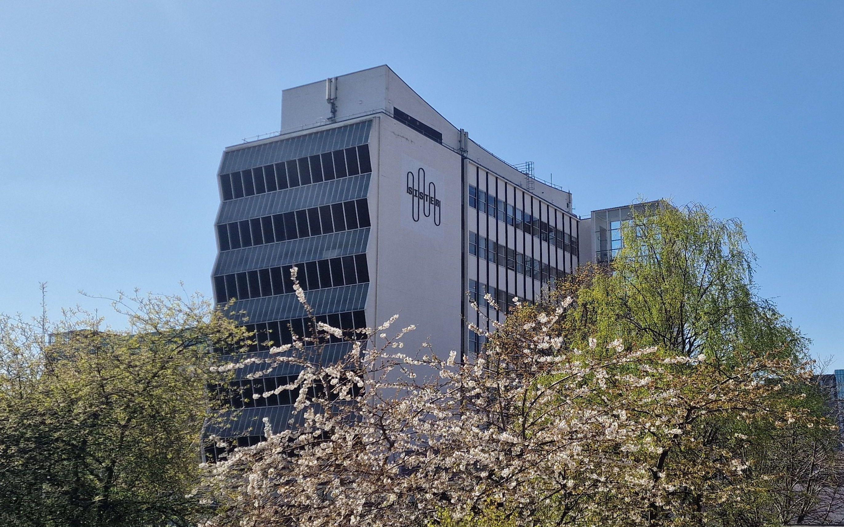 Exterior of the Renold building with the Sister logo on display and greenery