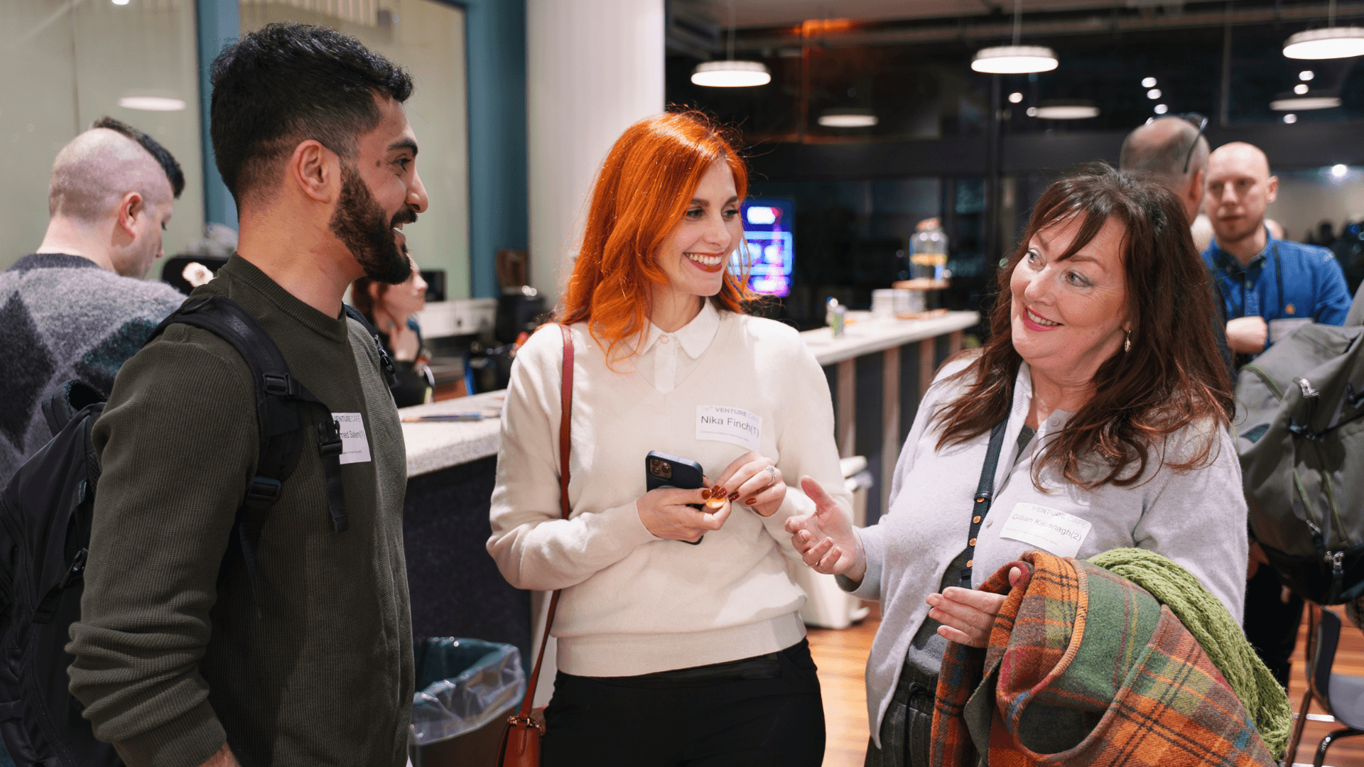 Three people wearing name badges stand around one another in conversation. They are all smiling and engaging with the discussion. 