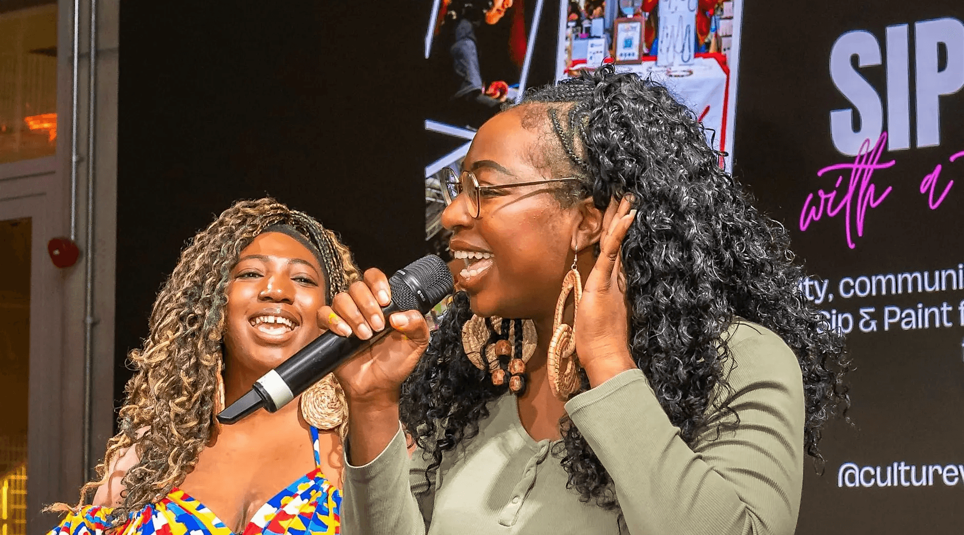 Two vibrant women take the mic as they introduce their creative event.