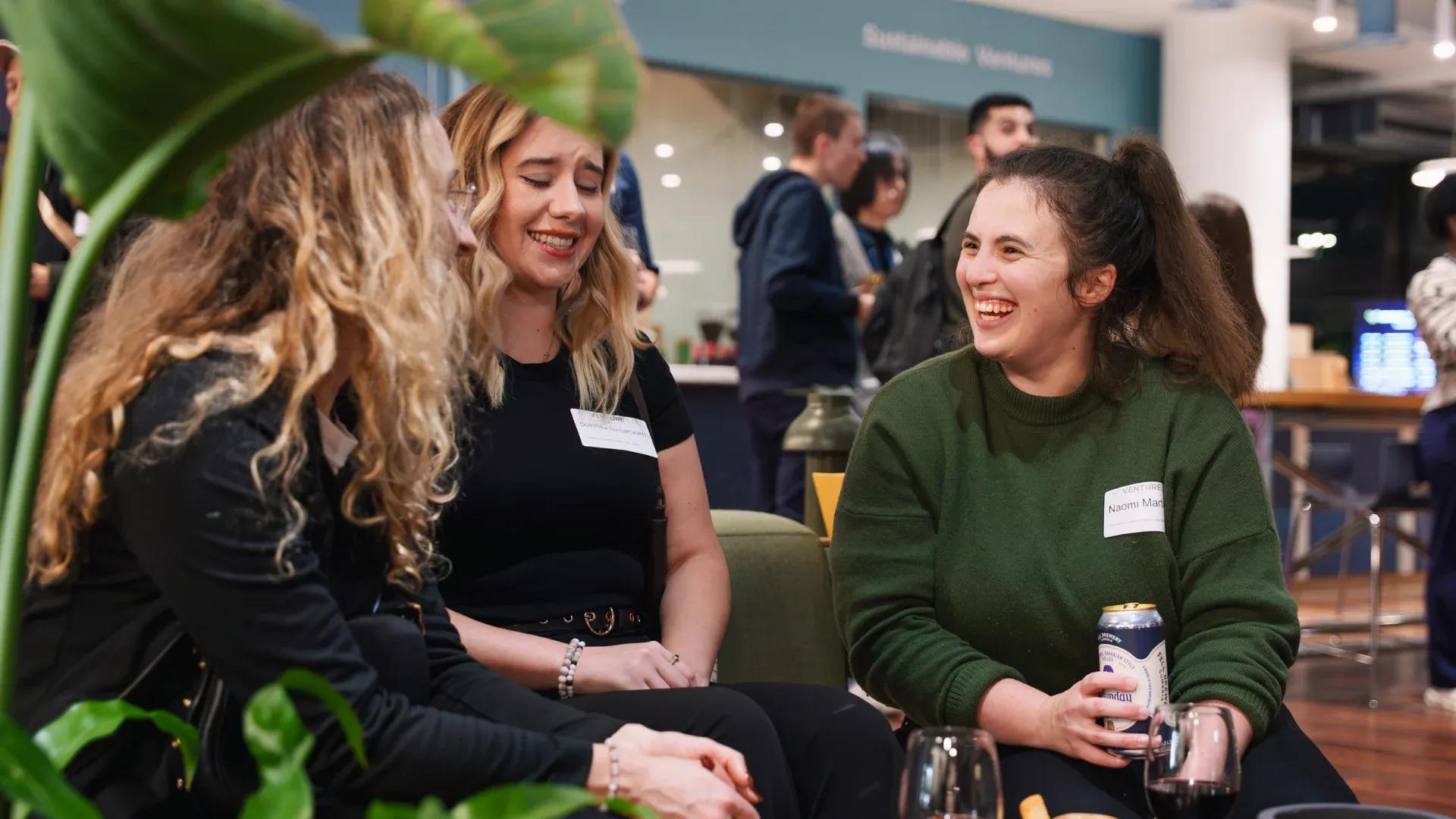 Three professional women sit together in Renold building of the Sister development. They are deep in conversation and laughing heartily.